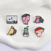 A collection of enamel pins featuring whimsical characters and funny phrases on a white surface.