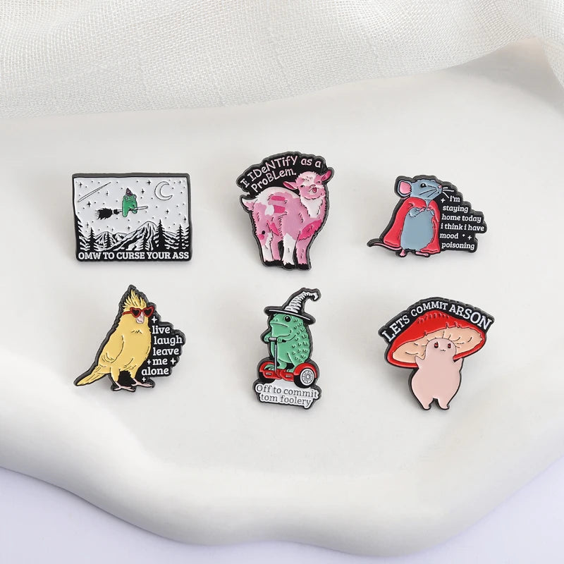 A collection of enamel pins featuring whimsical characters and funny phrases on a white surface.
