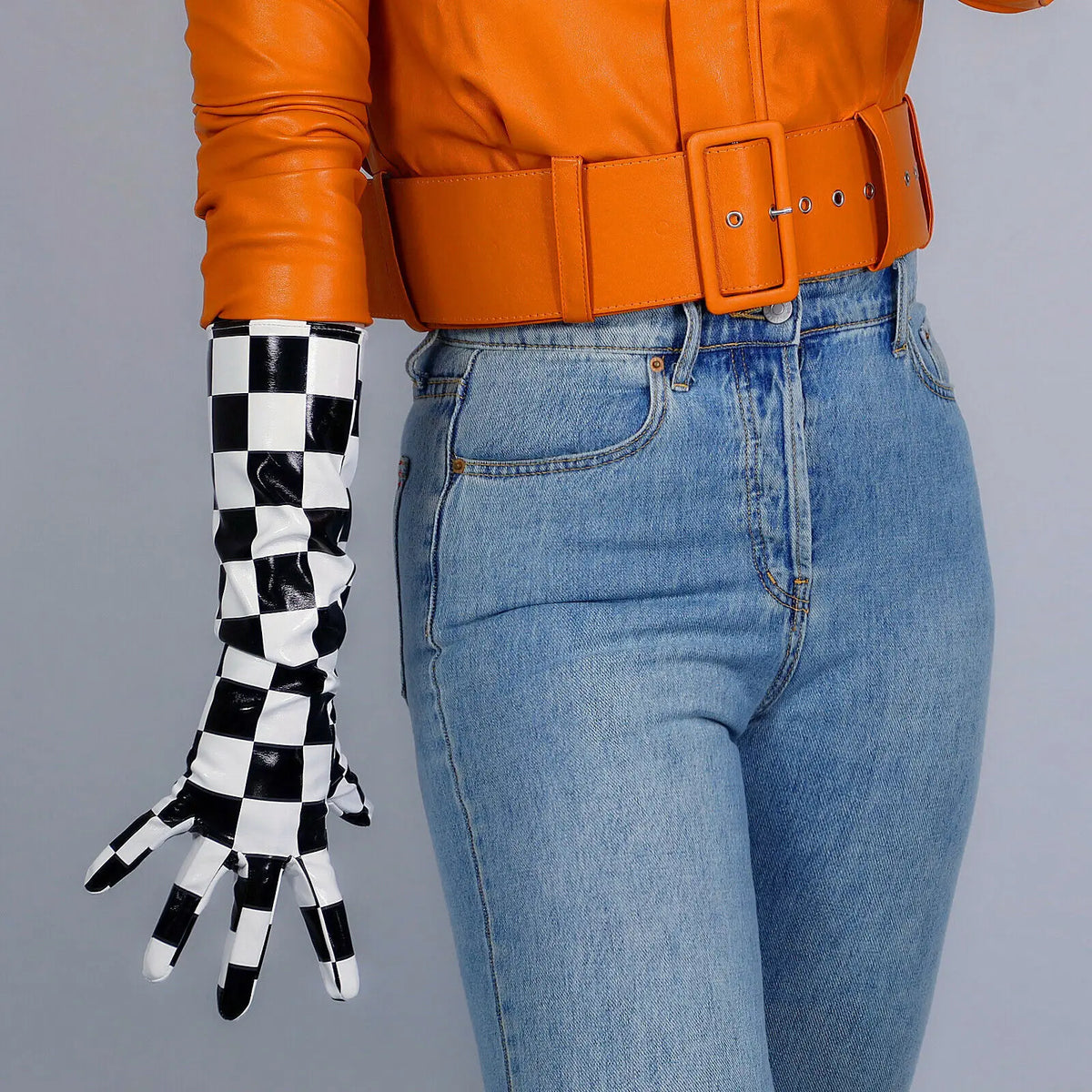 A close-up of a person wearing orange leather jacket, a wide belt, and black and white checkered latex gloves.