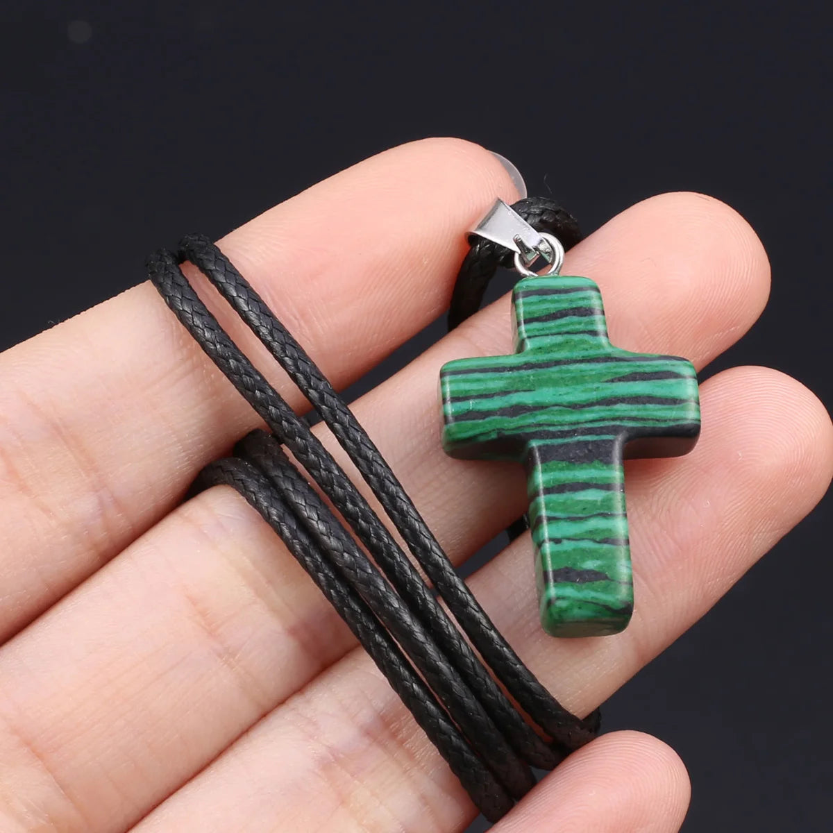 Eine Hand hält eine grüne und schwarze Tigerauge-Agat-Kreuz-Anhängerkette.