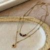 Gold chain necklace featuring a tiger eye sunflower pendant resting on a beige fabric surface.