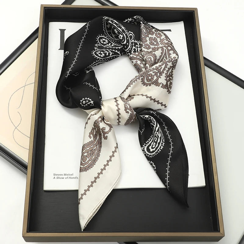 A black and cream patterned silk scarf tied in a bow displayed in a dark wooden frame.