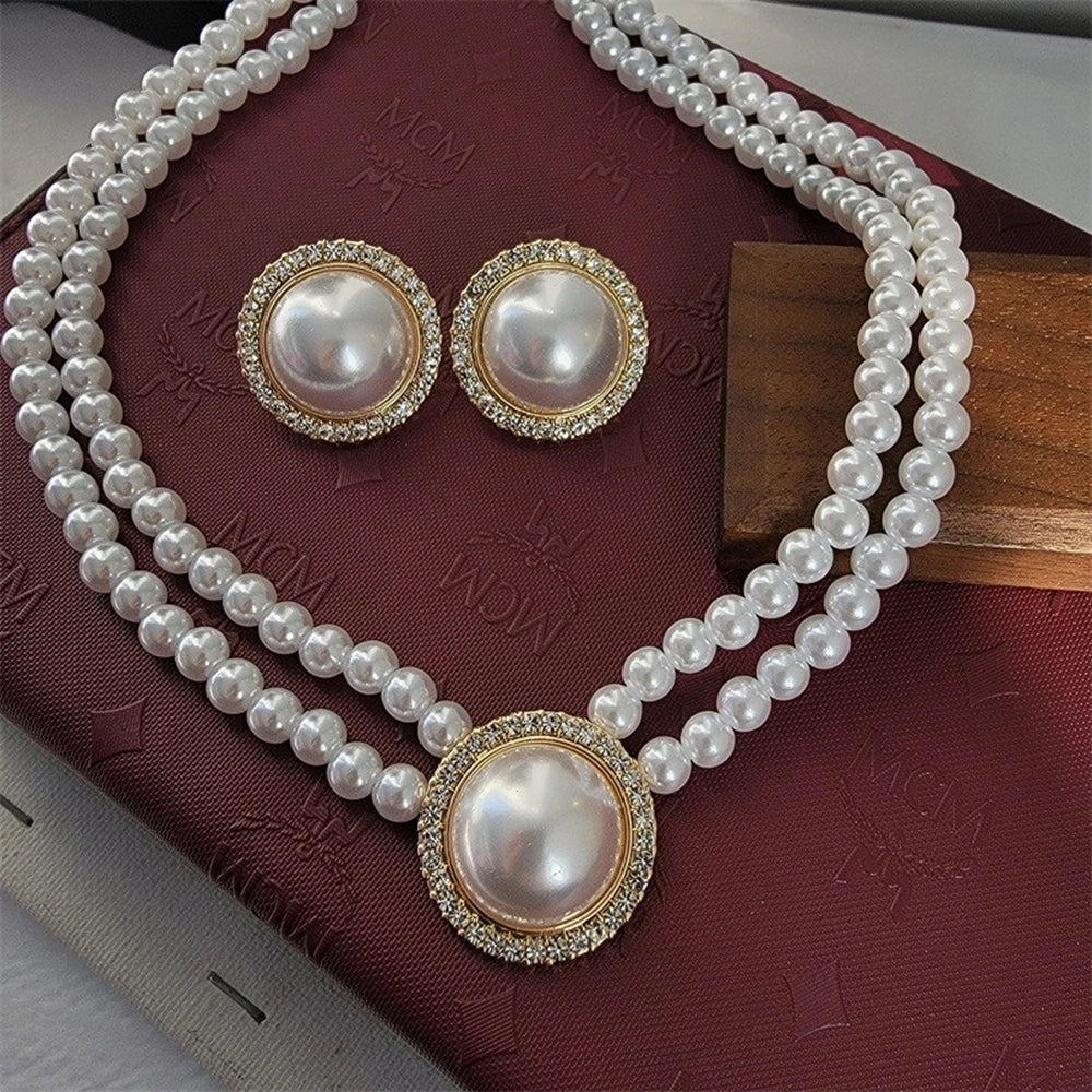 Un collier et des boucles d'oreilles de perles élégants avec accents de strass, présentés sur un velours rouge foncé.