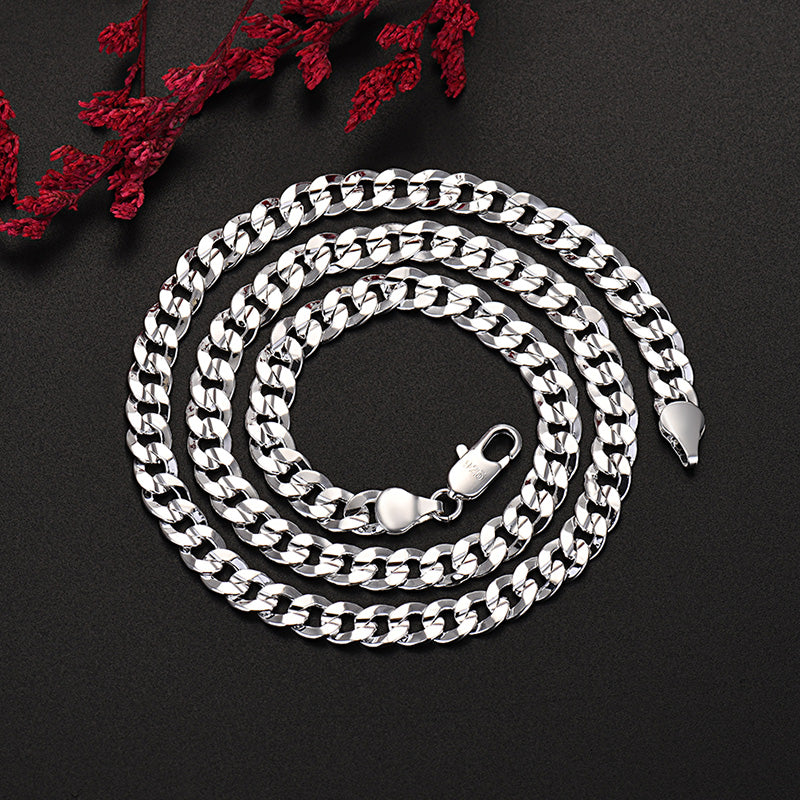 Un ensemble de collier et bracelet en argent enroulé sur une surface sombre avec des feuillages rouges en arrière-plan.