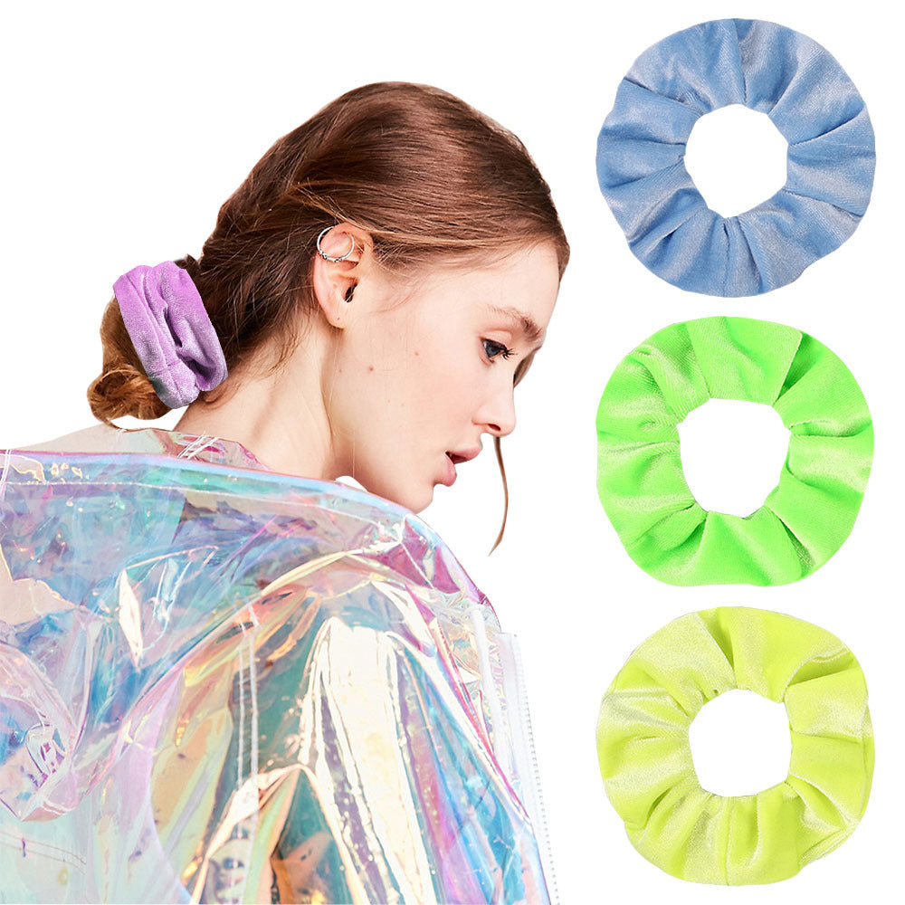 A woman is shown wearing a sheer, iridescent purple velvet scrunchie on her hair, with several scrunchies displayed separatel