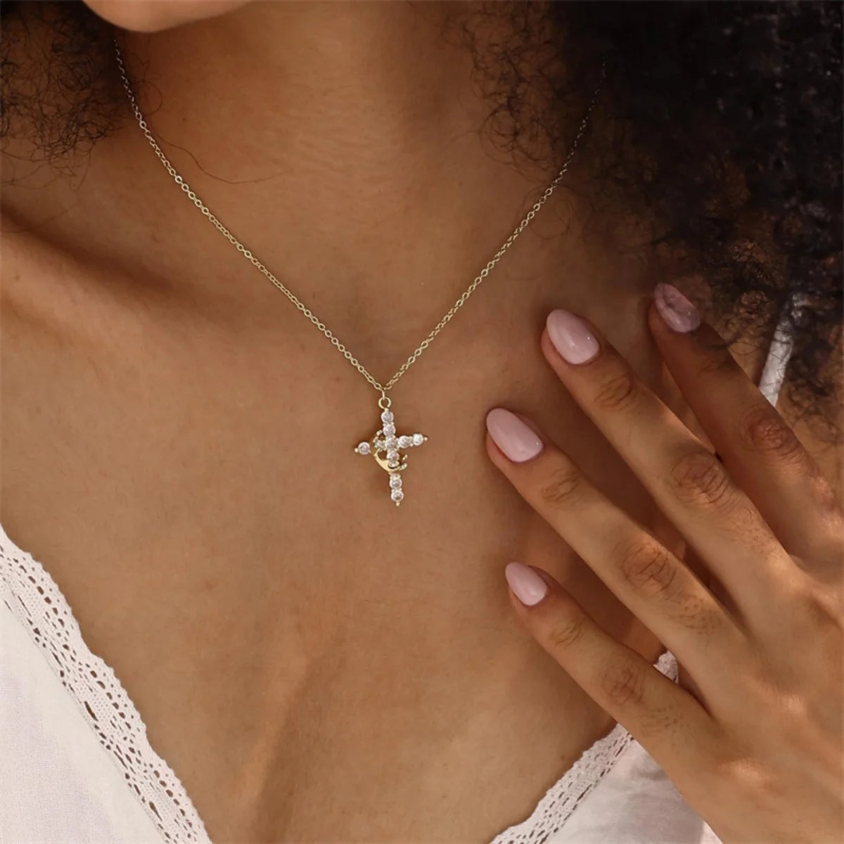 A close-up of a gold-toned cross pendant necklace worn around the neck against a skin tone.