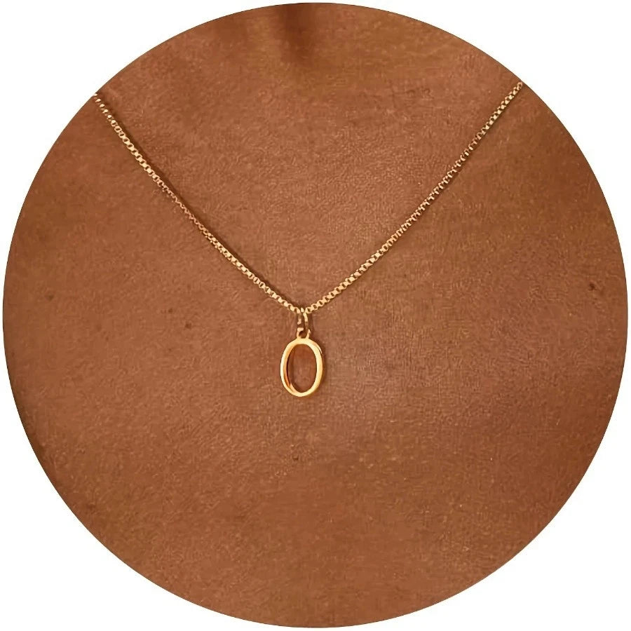 A delicate gold-plated stainless steel initial letter necklace with a simple circle charm displayed on a brown background.