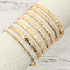 A stack of elegant gold hexagon star twist bangles displayed on a white fabric background.