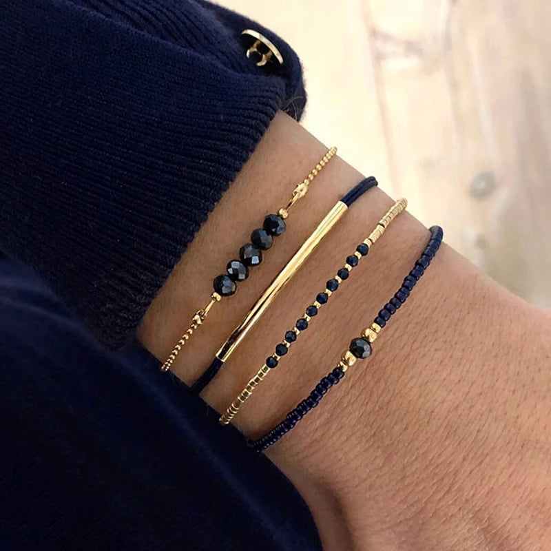 A close-up of a wrist wearing a stack of thin gold and black beaded bracelets.