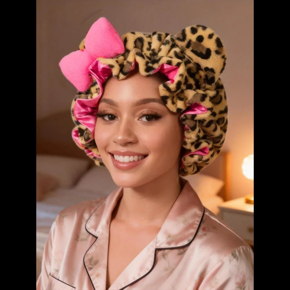 A woman wearing a leopard print hair drying cap with pink accents and a pink satin shirt.