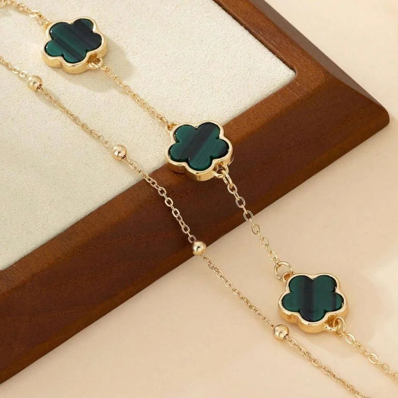 Gold chain anklet with a green five-leaf clover charm displayed on a wooden surface.
