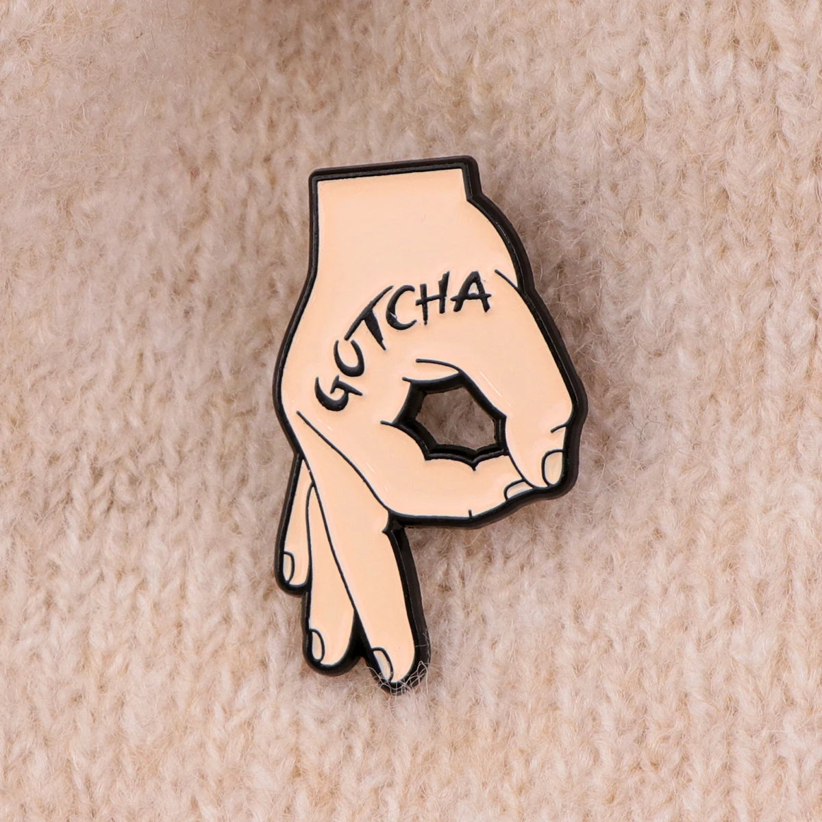 A gold-toned enamel pin shaped like a hand making a peace sign with the word GOTCHA inscribed on the palm.