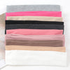 A stack of various colored knitted elastic headbands for hair and face, including pinks, blacks, grays, and beige tones.