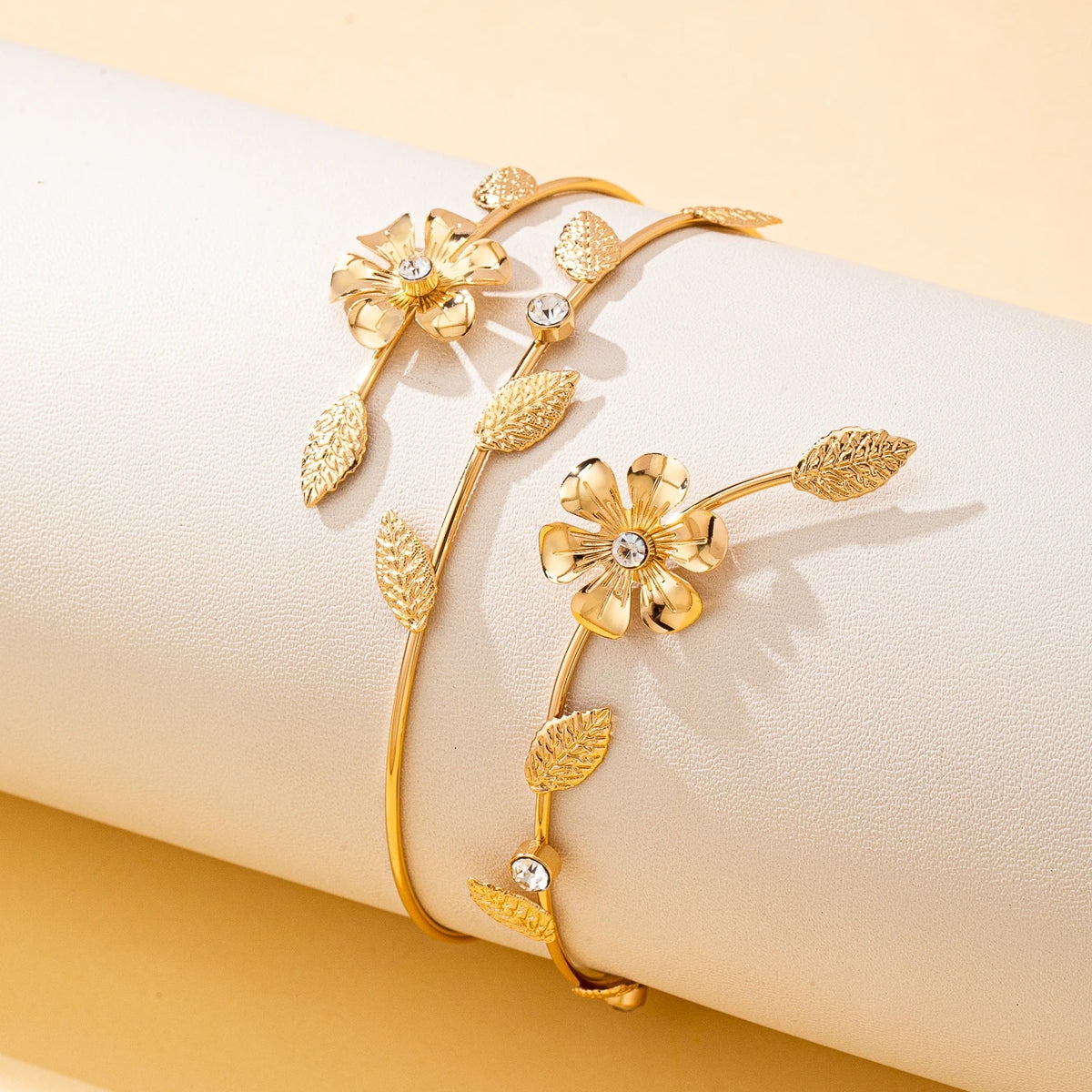 Gold floral vine arm bracelet with delicate leaves and small clear stones displayed on a cream background.