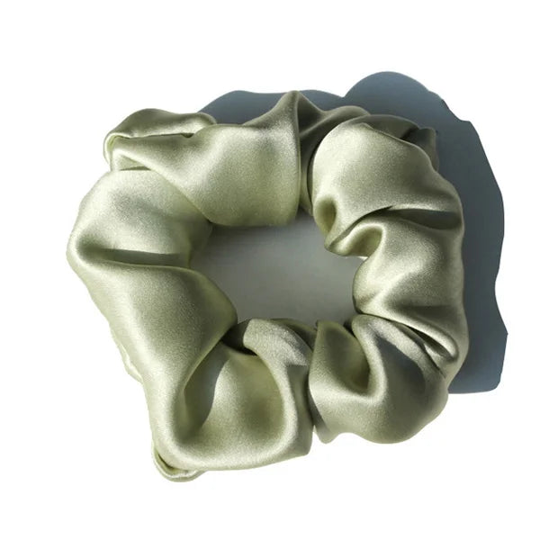 A close-up of a silk hair scrunchie in an olive green color, gathered and draped.