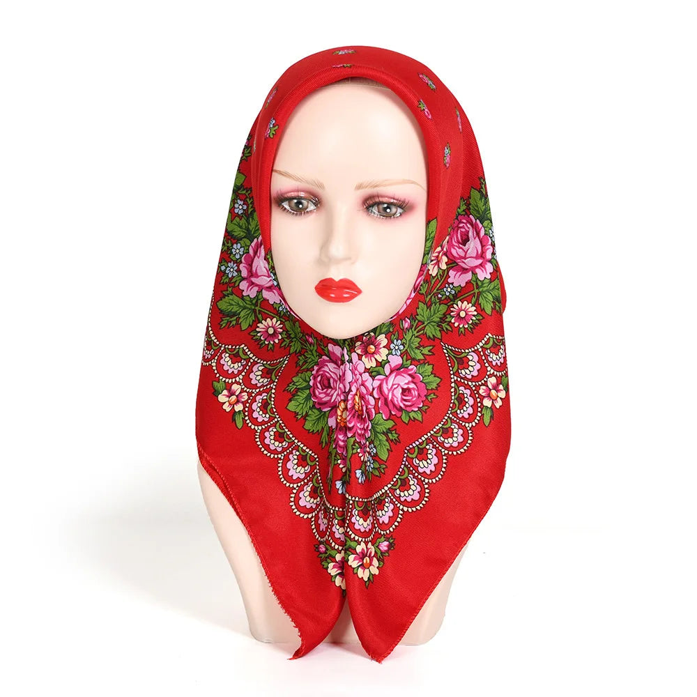 A woman's head wearing a vibrant red square scarf with a floral print and embroidery.