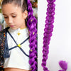 A close-up of a woman wearing a white top and gold pants, with a long purple braided hair extension hanging down.