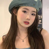 A young woman wearing a teal retro washed cotton denim beret hat and a blue top.