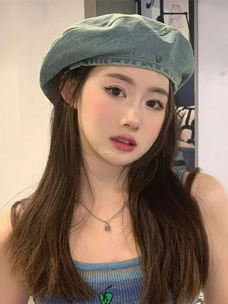 A young woman wearing a teal retro washed cotton denim beret hat and a blue top.