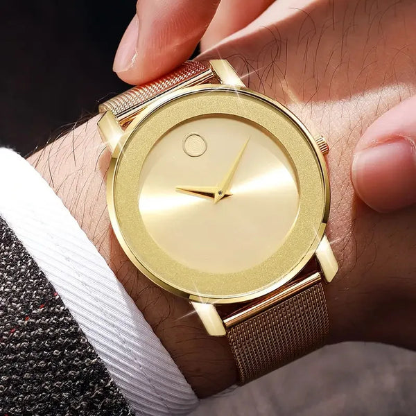 A close-up of a gold-toned quartz wristwatch with a white face and a rose gold mesh strap worn on a wrist.