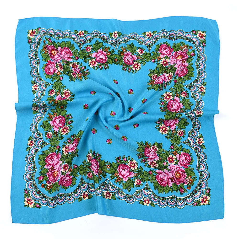 A light blue square scarf featuring a detailed floral print with pink, green, and white accents.