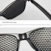 A pair of black vision correction pinhole glasses shown in close-up, demonstrating three-dimensional cutting and a perforated