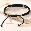 Schwarzes geflochtenes Armband mit silbernem Anhänger auf heller Oberfläche.
