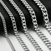 A close-up of several silver stainless steel hip hop Cuban chain necklaces arranged diagonally against a dark background.