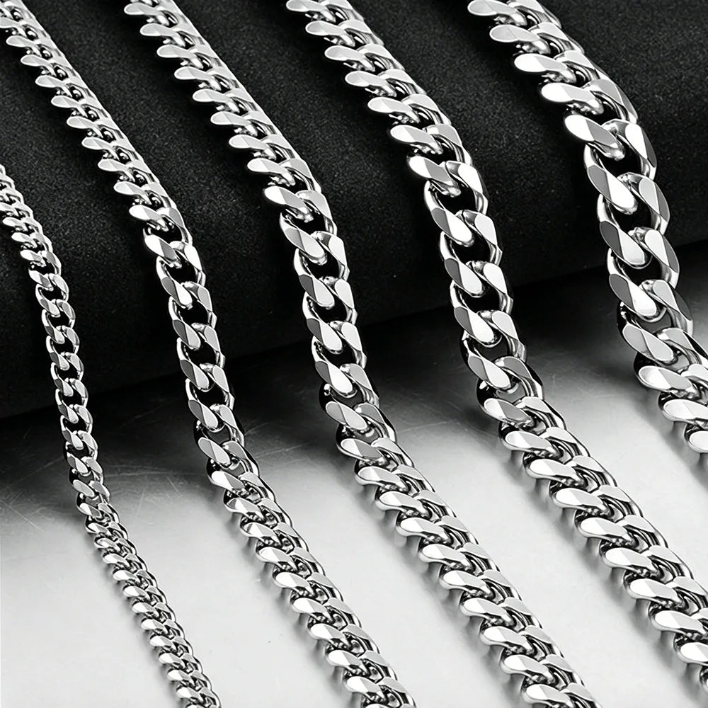 A close-up of several silver stainless steel hip hop Cuban chain necklaces arranged diagonally against a dark background.