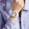 A close-up of a woman wearing a white quartz fashion watch with a silicone strap on her wrist, paired with a light purple shi