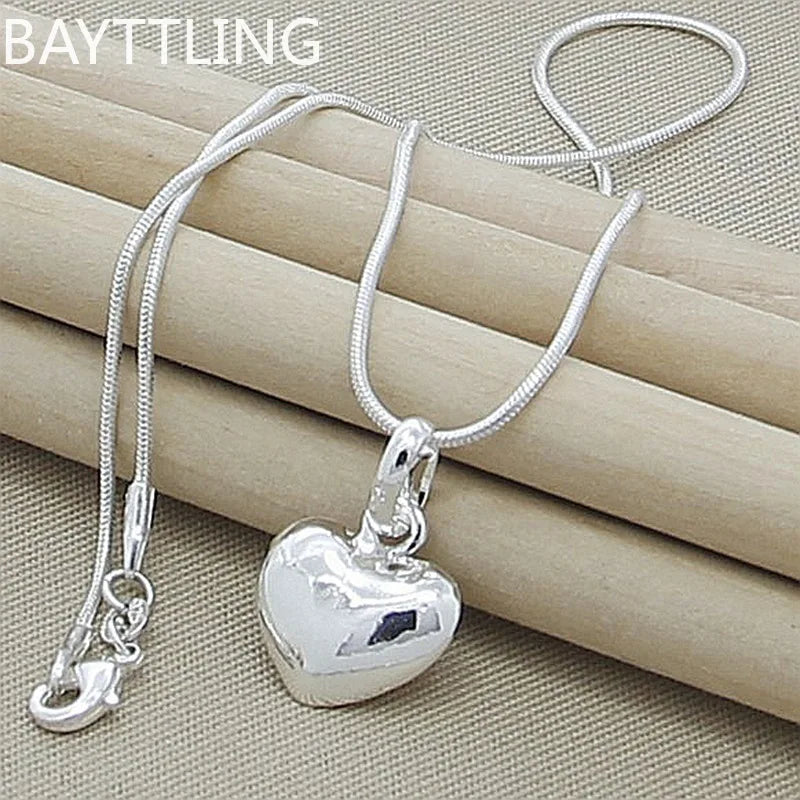 A silver heart snake necklace is displayed on a beige fabric background.