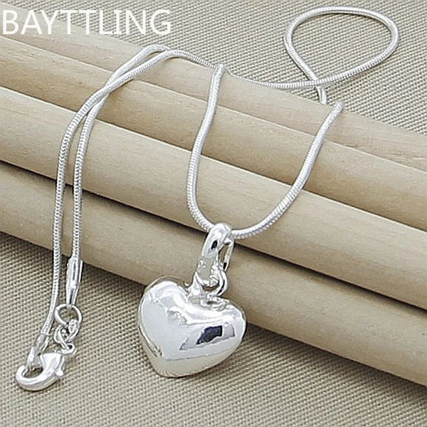 A silver heart snake necklace is displayed on a beige fabric background.
