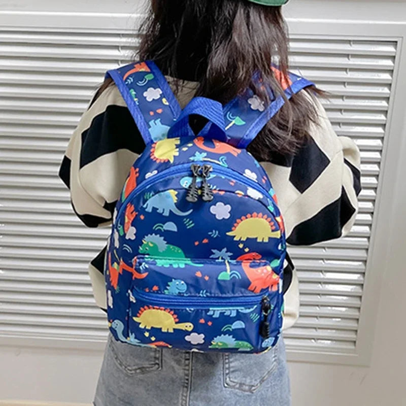 A blue backpack featuring a cute dinosaur and unicorn pattern worn by a person.