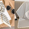A striped silk scarf in black and white with a rose design is displayed on a beige blazer and draped over a sofa.