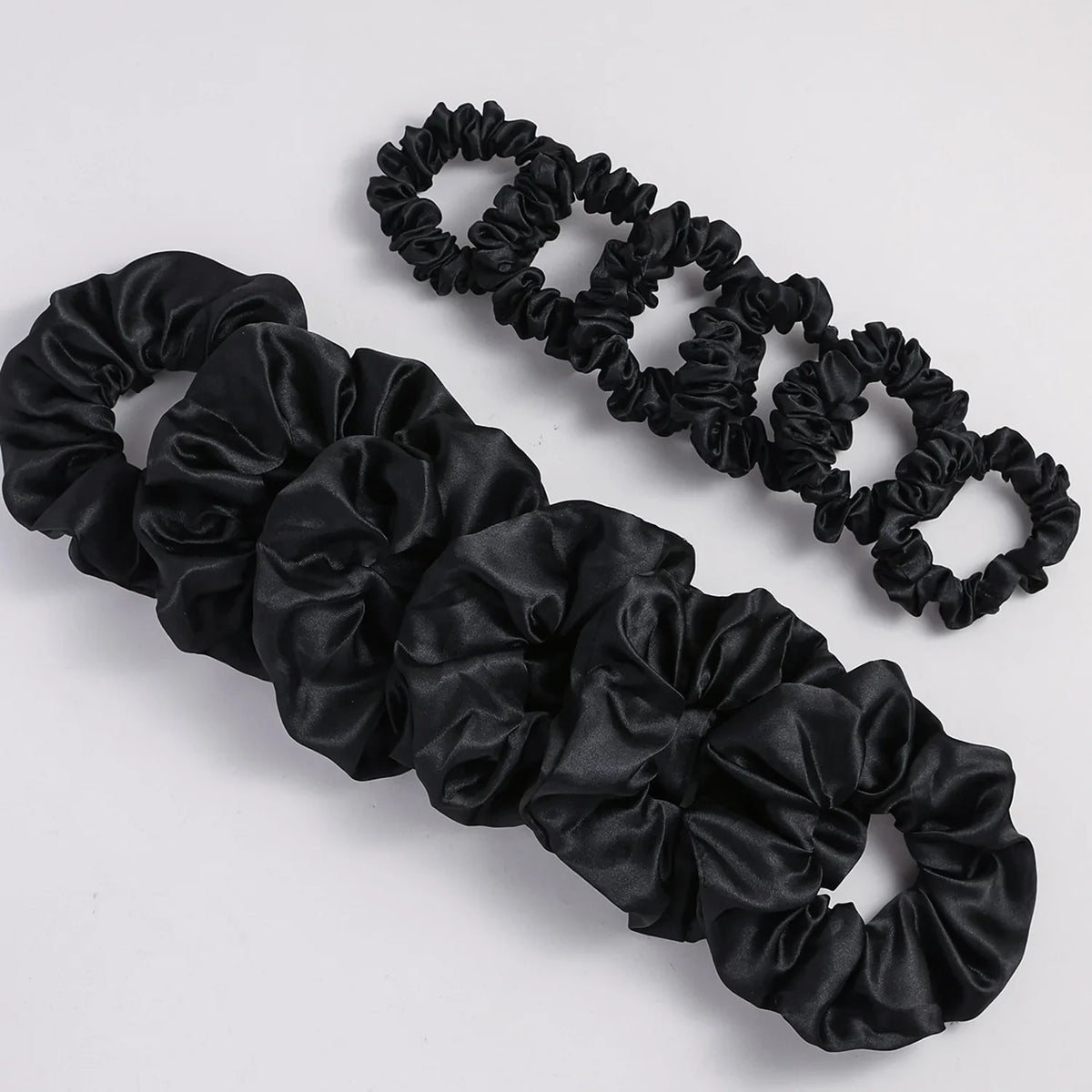 Black satin elastic hair ties in a ruffled design, shown as two separate strands.