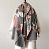 A beige knit sweater is draped with a plaid cashmere feel scarf and shawl wrap featuring pink, gray, and black geometric patt
