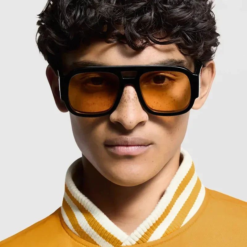 Modelo masculino vistiendo gafas de sol cuadradas retro de doble puente negras con lentes ámbar y una camisa a rayas amarilla
