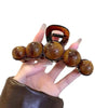 A hand holds an elegant acrylic pearl hair claw clip with a dark amber finish.