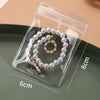 A clear self-sealing jewelry storage pouch containing a pearl necklace is displayed on a green plate.