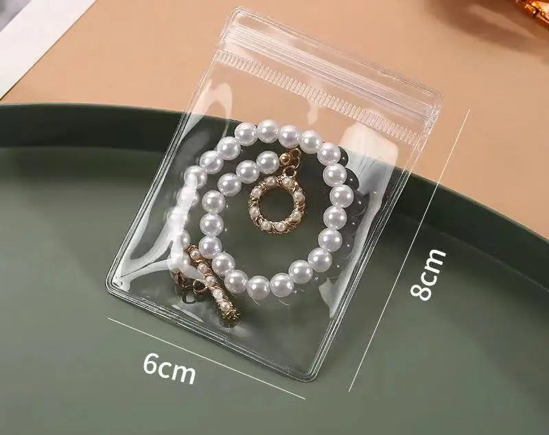 A clear self-sealing jewelry storage pouch containing a pearl necklace is displayed on a green plate.