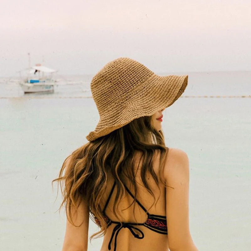A woman wearing a hand-woven straw visor hat, looking over her shoulder near the sea.