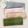 A set of four knitted hair bands in shades of gray, pink, beige, and olive green laid on a light background.