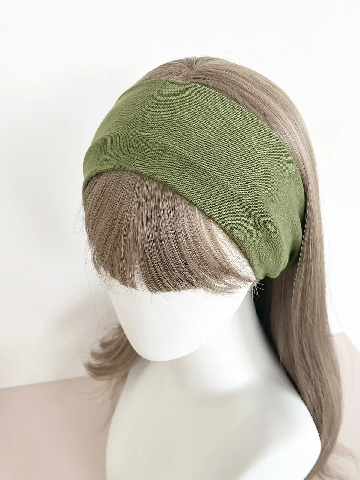 A model is wearing a olive green knitted hair band on her head.