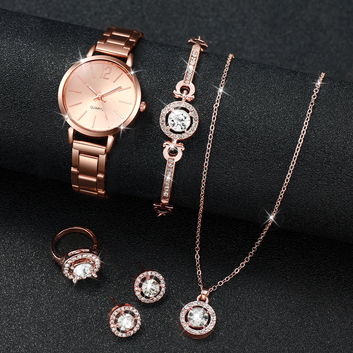 A set of rose gold quartz wrist watch and various diamond jewelry pieces displayed on a dark surface.