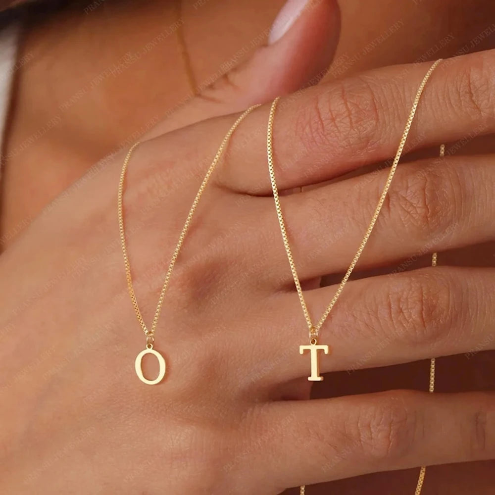 A close-up of a hand wearing a delicate gold initial letter necklace with the letter O and T.