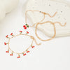 A set of gold-colored anklets featuring small red cherry beads and gold chains displayed on a white surface.