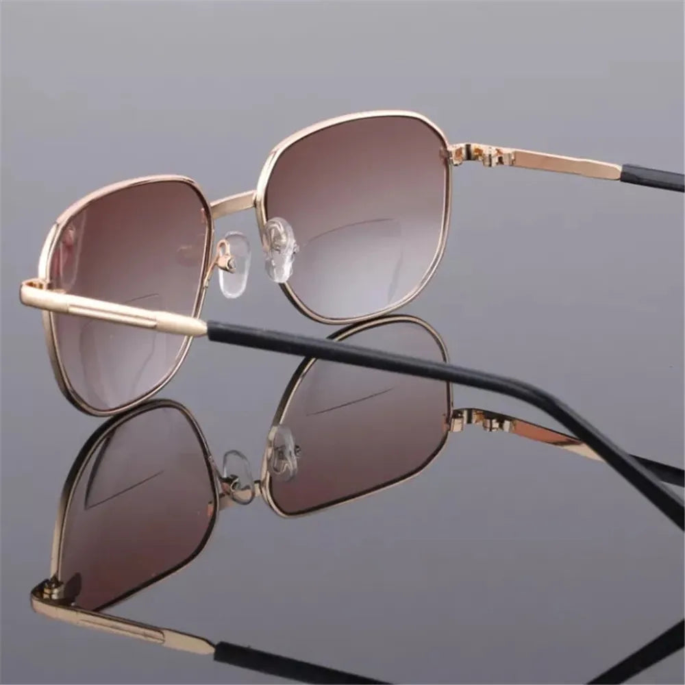 A pair of gold-framed sunglasses with brown lenses resting on a gray background.