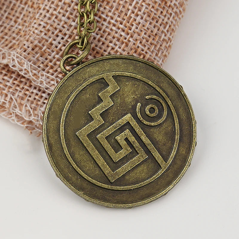 A round, antique brass pendant featuring a stylized pentacle design, suspended from a gold-colored chain.