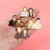 Une main tient plusieurs broches émaillées représentant des personnages de Twilight