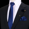 Chaqueta de traje negra con camisa blanca, corbata de seda azul y pañuelo de bolsillo y prendedor de seda azul oscuro.